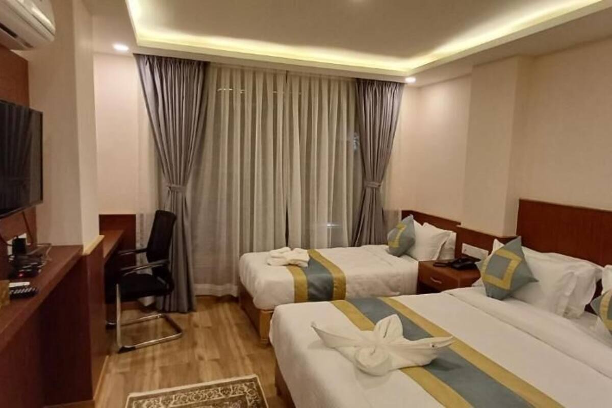 A hotel room with two beds, a desk with a television, and a window with curtains.