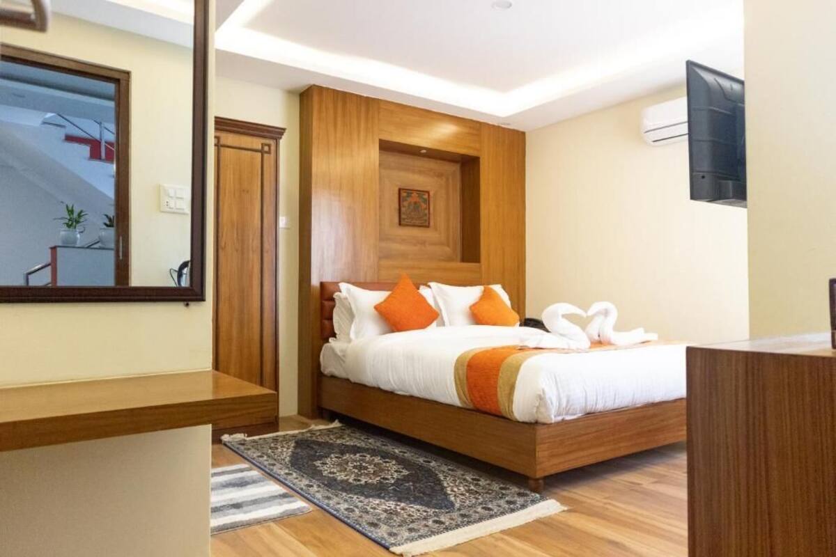 A modern hotel room with a wooden bed, a large mirror, and a flat-screen TV.