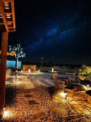 An outdoor seating area with stone flooring and wooden furniture under a night sky with visible stars and the Milky Way. - Amazing 3-bedroom house Large Pool ,Cold plunge HotTub  WiFi, Joshua Tree NP,❄️AC (Yucca Valley)