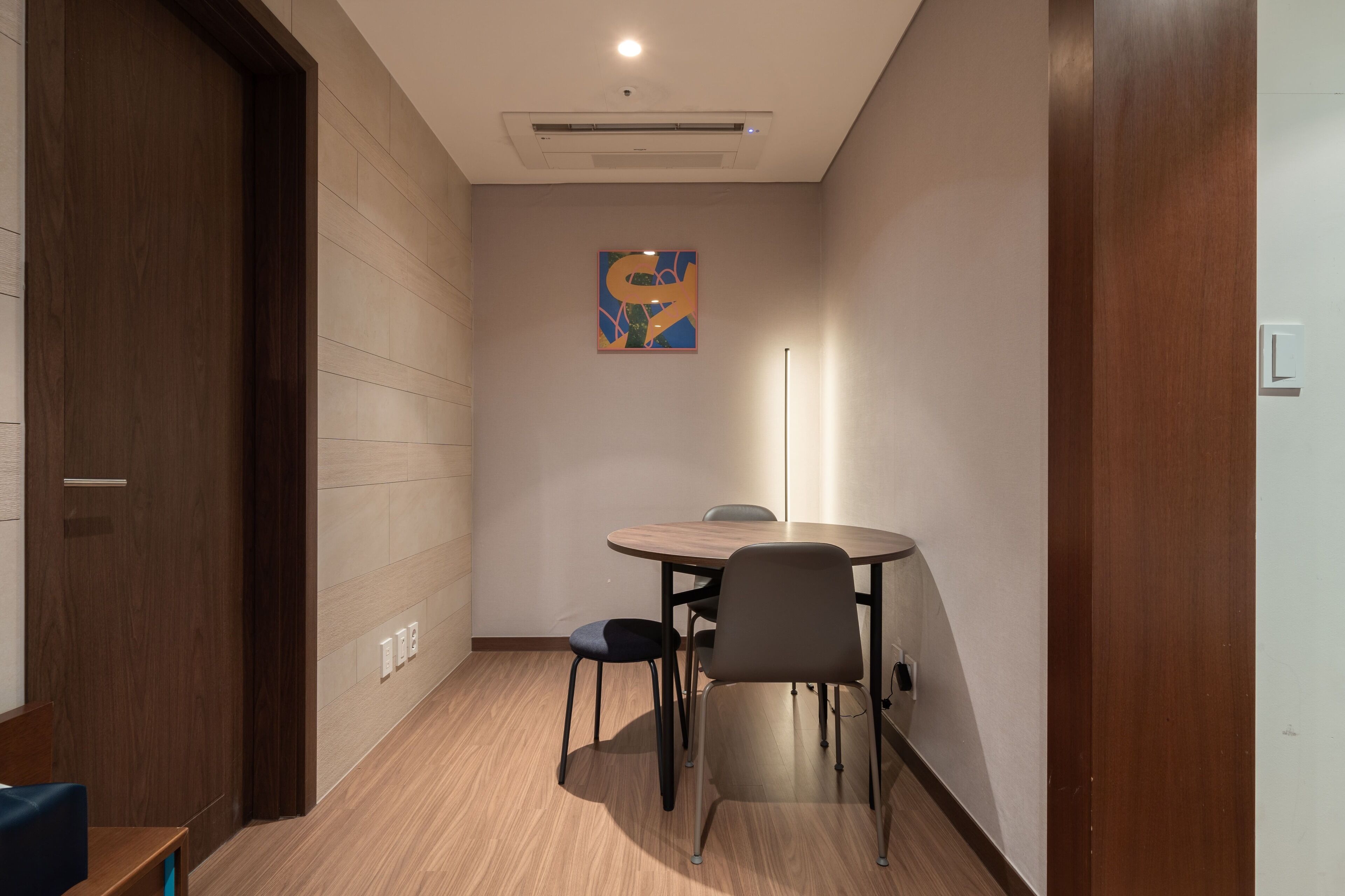 A small, modern room with a wooden floor, a round table with chairs, and a painting on the wall.