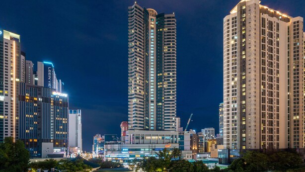 Un paisaje urbano nocturno con rascacielos, incluyendo una torre destacada con forma curva y otra con techo plano.