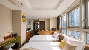 Habitación de hotel con dos camas, un escritorio, una silla, una ventana con vista a la ciudad y una puerta que da a un pasillo.