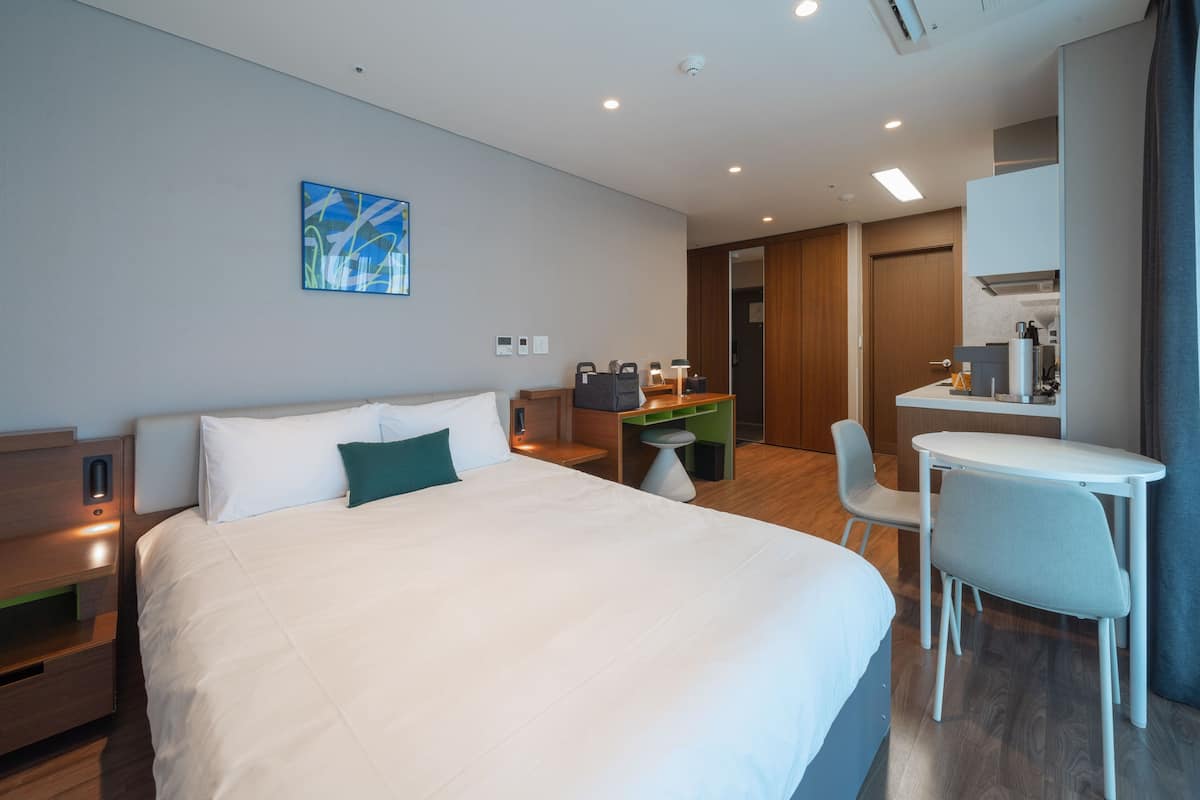 Una habitación de hotel moderna con una cama grande, un escritorio, una silla y una pequeña kitchenette.