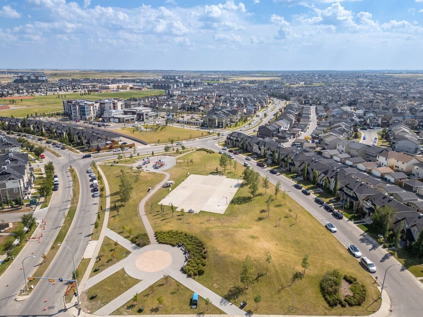 Een woongebied met een groot open veld, mogelijk een park of sportveld, omringd door huizen en enkele winkelgebouwen.