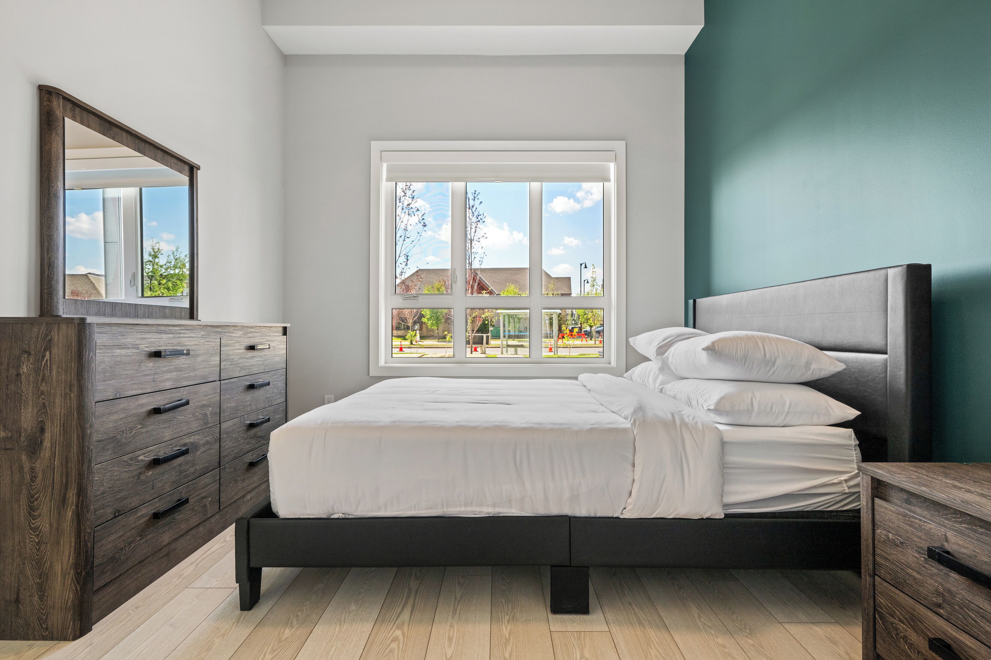 Ein Schlafzimmer mit einem Bett, einer Kommode und einem Fenster mit Blick auf ein Haus und Bäume.