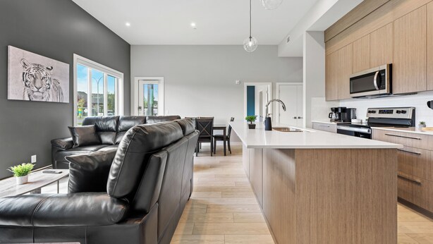 A modern kitchen with a central island, wooden cabinets, and a microwave. - Ground-Level 3BR Condo w/ UG Parking, Lawn Access (Northeast)