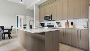 A modern kitchen with wooden cabinets, a central island, and a microwave. - Ground-Level 3BR Condo w/ UG Parking, Lawn Access (Northeast)