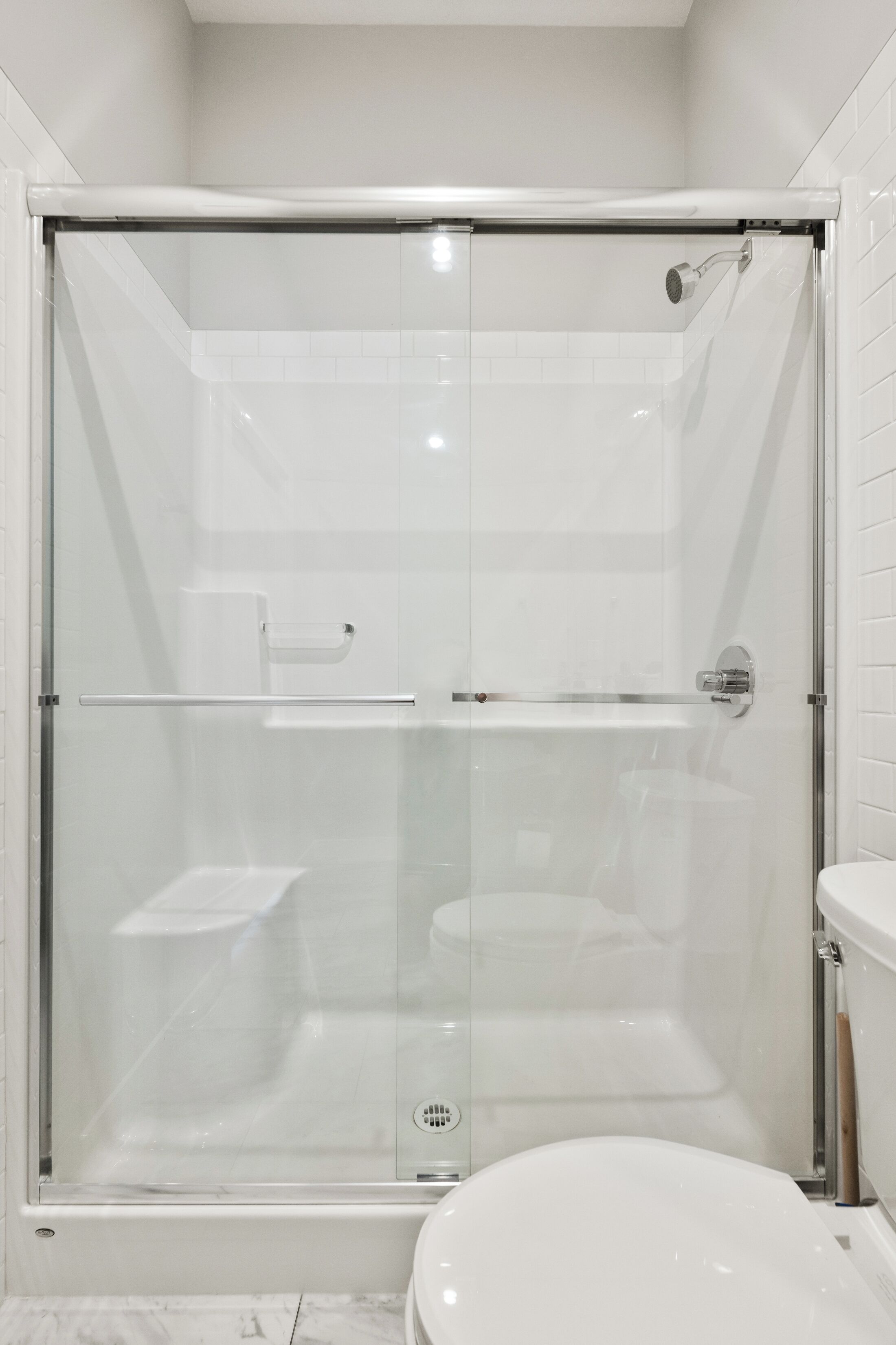 A modern bathroom with a glass-enclosed shower, a white toilet, and a marble floor.