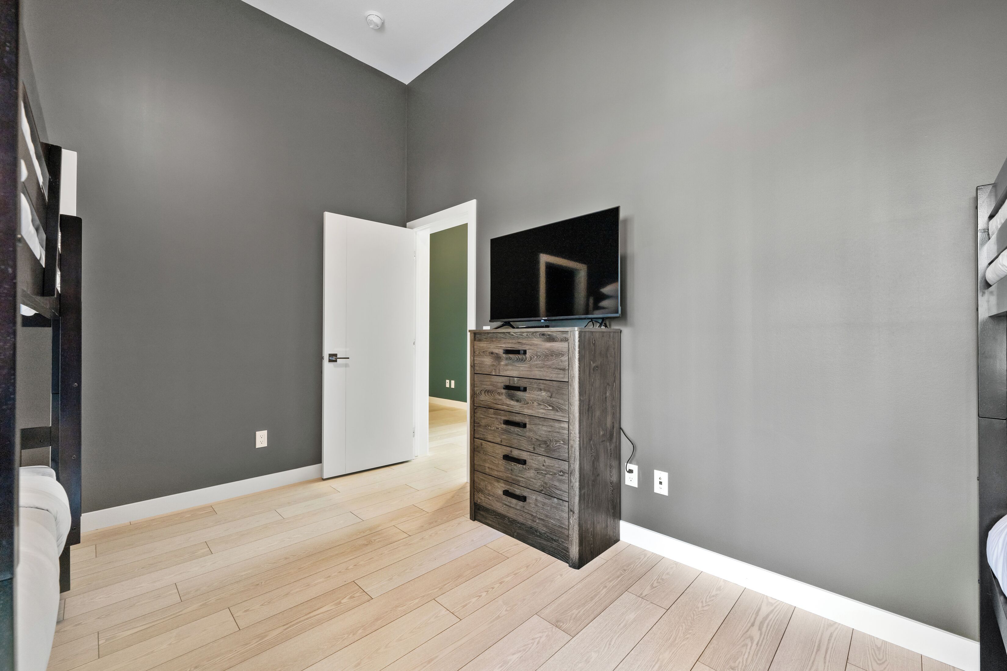 Ein modernes Zimmer mit grauen Wänden, Holzboden, einem Einbauschrank und einem flachbildfernseher an der Wand.