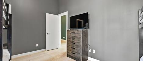 Ein modernes Zimmer mit grauen Wänden, Holzboden, einem Einbauschrank und einem flachbildfernseher an der Wand.