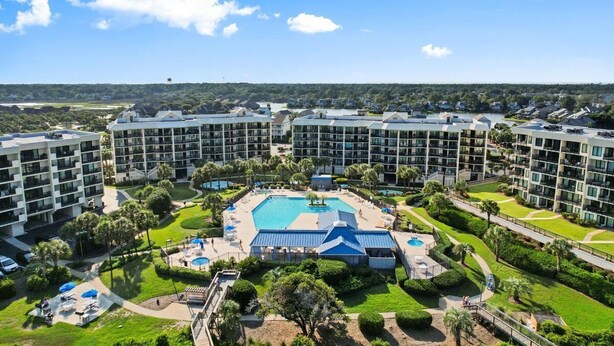 A hotel with multiple buildings, a central swimming pool, and surrounding greenery.
