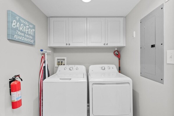 A laundry room with two white washing machines, a fire extinguisher, and a sign on the wall.