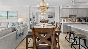 A modern kitchen with a central island, a dining area with a chandelier, and a living room with a sofa and a lamp.