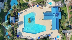 An aerial view of a resort with a large central pool, multiple smaller pools, and a variety of outdoor seating areas.