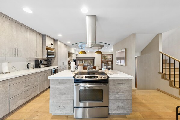 A modern kitchen with a central island, stainless steel appliances, and a view to the living area.
