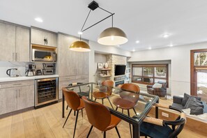 A modern kitchen with built-in appliances, a dining area with glass-top table and leather chairs, and a cozy living space with a fireplace.