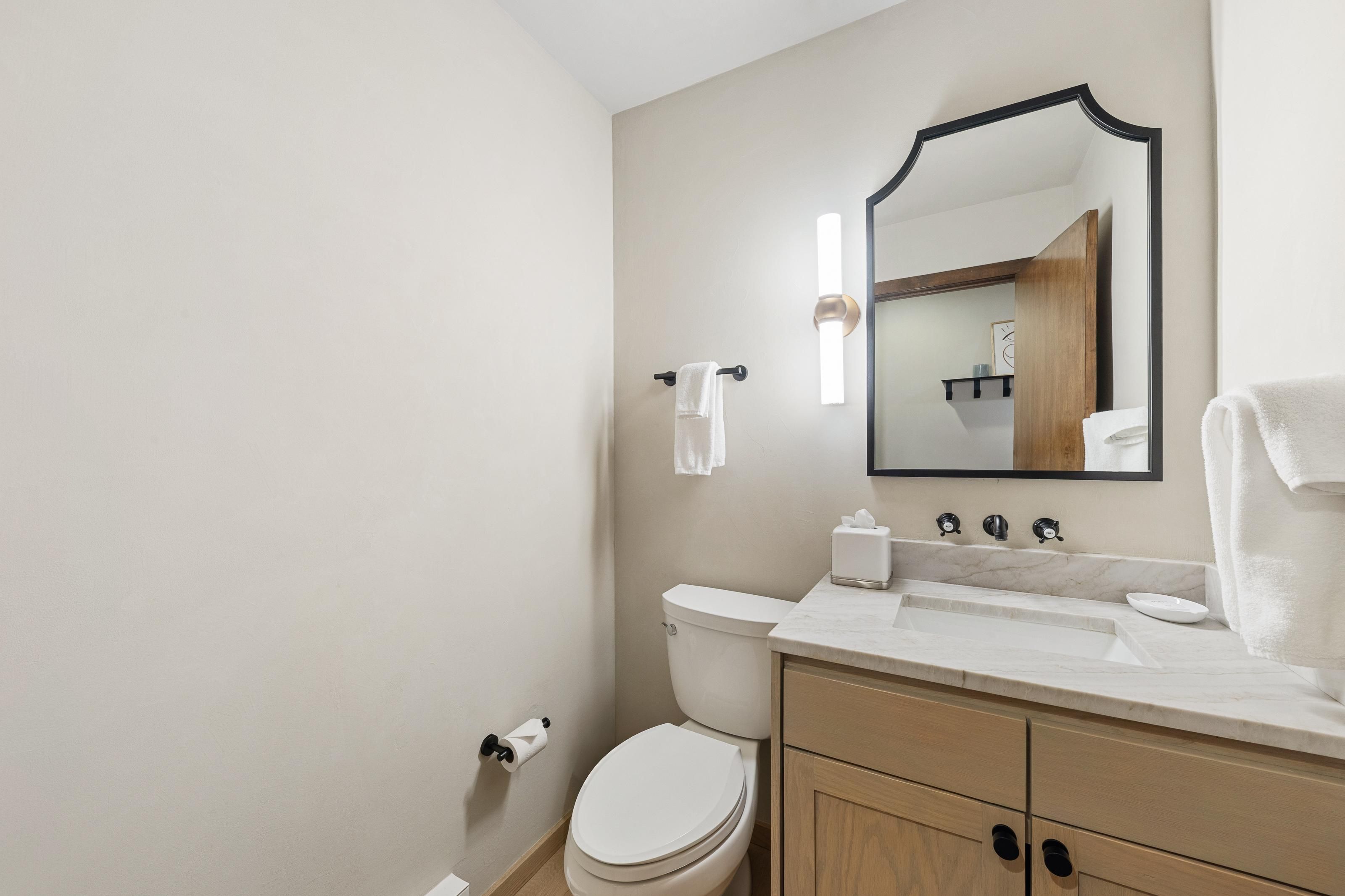 A bathroom with a toilet, sink, mirror, towel rack, and a towel on the counter.