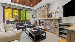A modern living room with a stone fireplace, leather sofas, and a flat-screen TV.