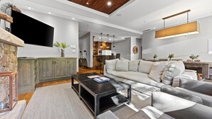 A modern living room with a stone fireplace, a large flat-screen TV, a grey sofa, and a black coffee table.