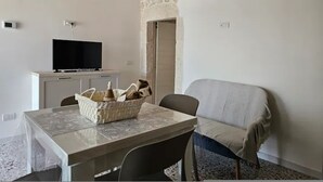 Una habitación con pared de piedra, televisión sobre un mueble, una mesa con una cesta y una silla.