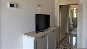 Una habitación con una televisión sobre un mueble, una pared de piedra y una puerta que da a otra habitación.