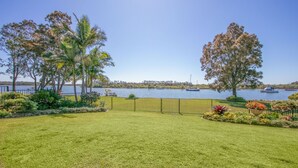 A well-maintained lawn with a metal fence, palm trees, and a view of boats on a lake.