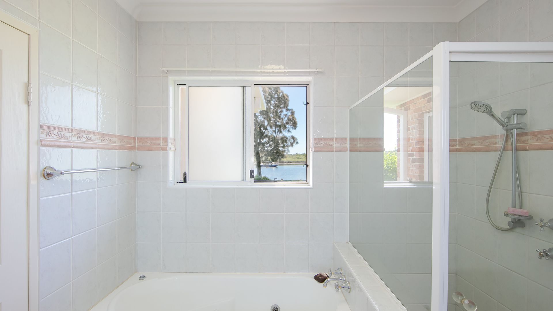 Une salle de bain moderne dotée d’une baignoire, d’une douche et d’une fenêtre donnant sur un arbre et une étendue d’eau.