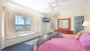 A hotel room with a large bed, a ceiling fan, a television, a mirror, and a view of the water outside.