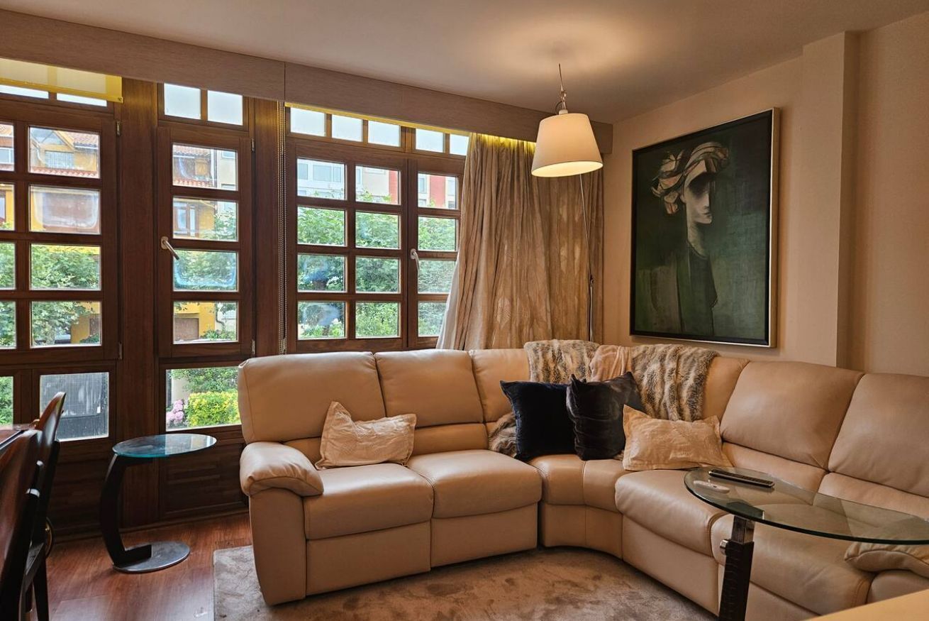 A modern living room with a beige sectional sofa, a glass coffee table, and a painting on the wall.