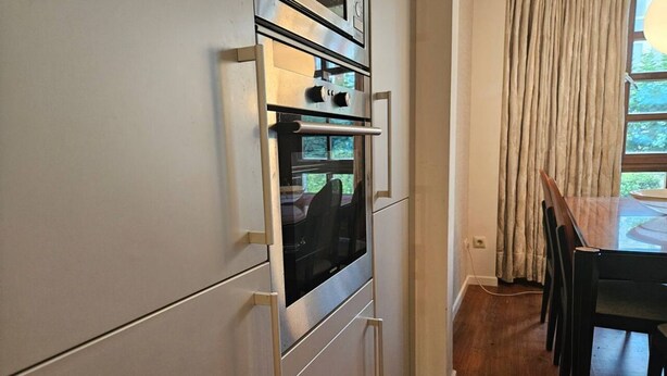 Une cuisine équipée d’un four encastré, une table à manger avec des chaises et une fenêtre avec des rideaux.