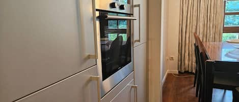 A kitchen with a built-in oven, a dining table with chairs, and a window with curtains.