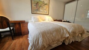 Une chambre à coucher avec un lit double, une table de chevet, une chaise, une commode en bois et un tableau accroché au mur.