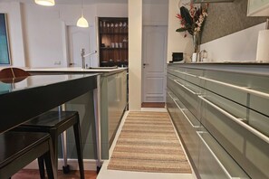 A modern kitchen with a central island, stainless steel appliances, and a wooden dining table. - 15A07 Sablón 2 (Llanes)