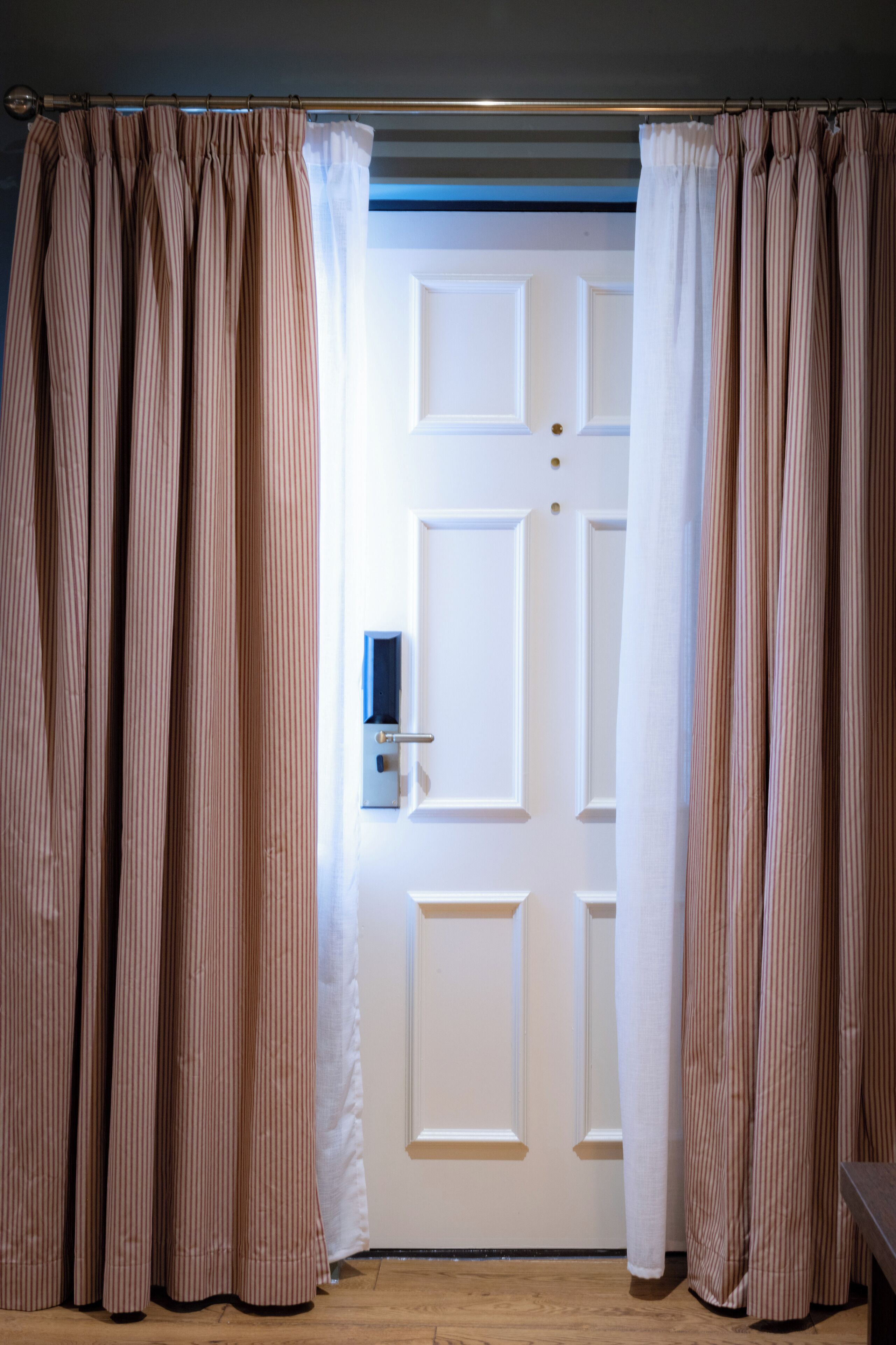A room with a closed door, striped curtains, and a wooden floor.