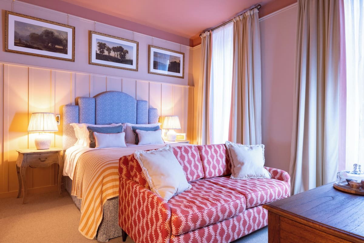 A hotel room with a bed, two bedside tables with lamps, a sofa, and a wooden side table.