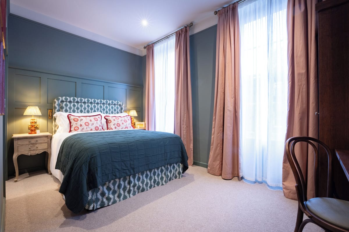 A bedroom with a bed, nightstands, a chair, and curtains.