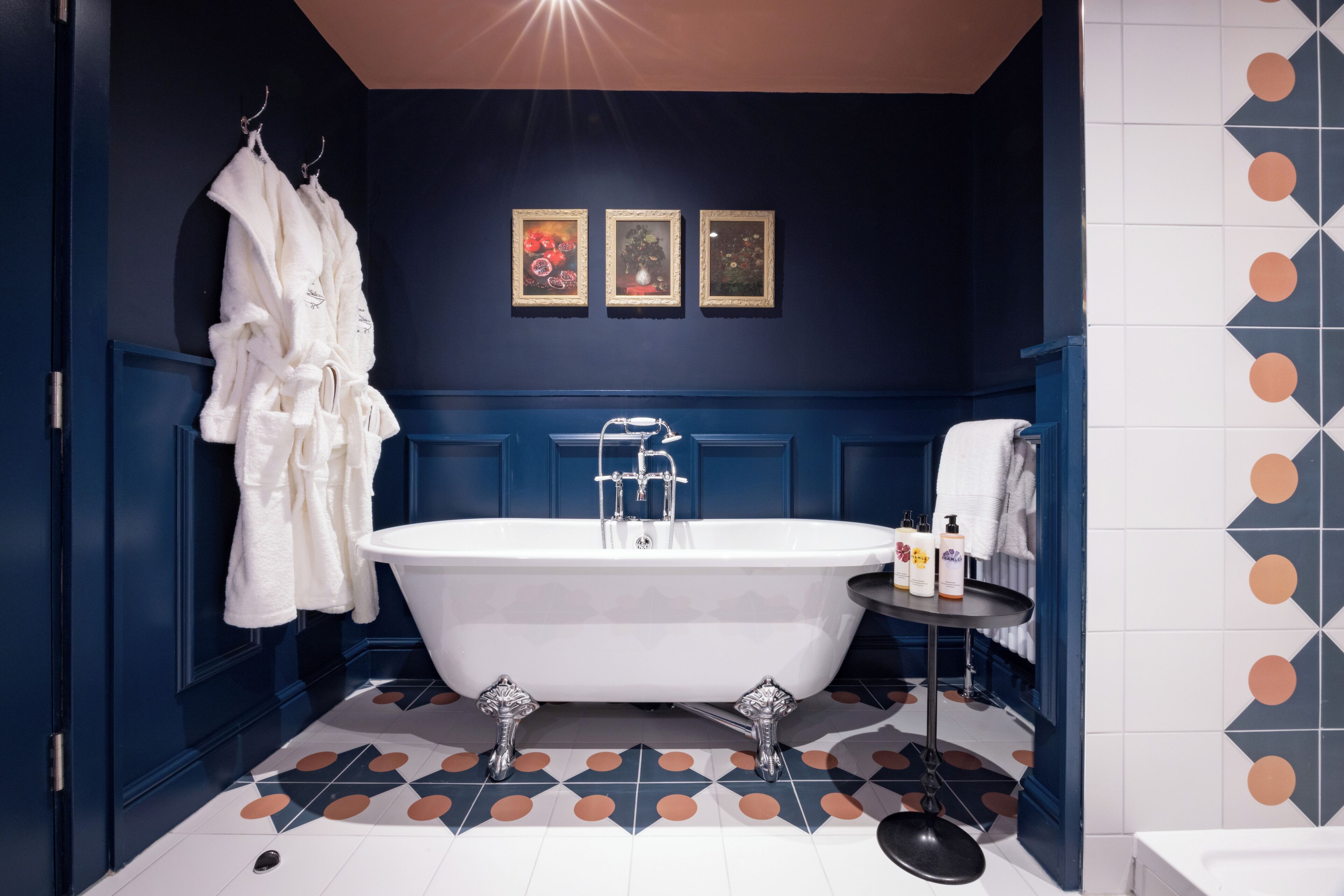 Un bagno con una vasca da bagno bianca, indipendente, un porta asciugamani con asciugamani bianchi e un piccolo tavolo con articoli da toilette.