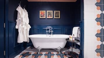Un bagno con una vasca da bagno bianca, indipendente, un porta asciugamani con asciugamani bianchi e un piccolo tavolo con articoli da toilette.