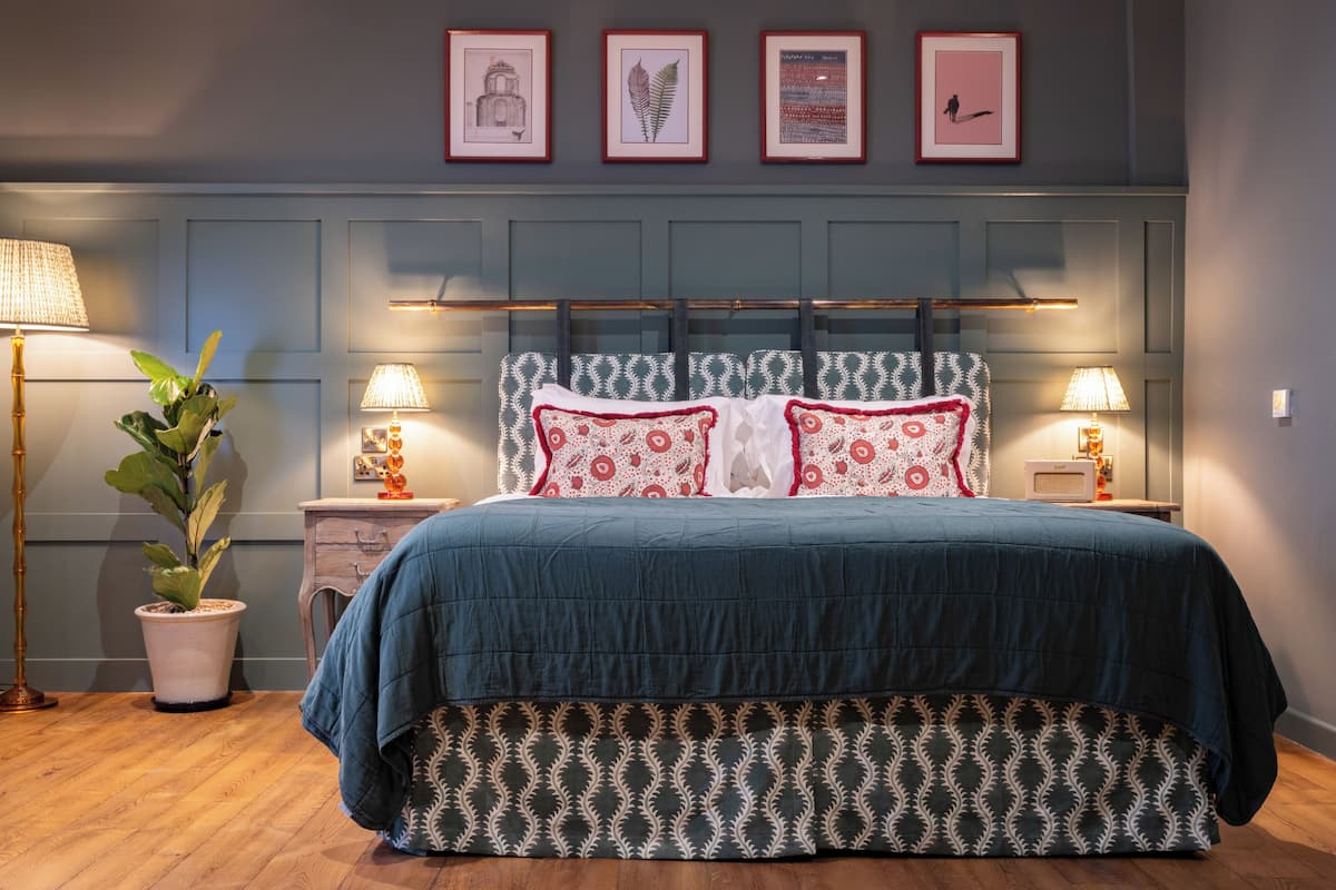 A bedroom with a bed, bedside lamps, a potted plant, and framed artwork on the wall.