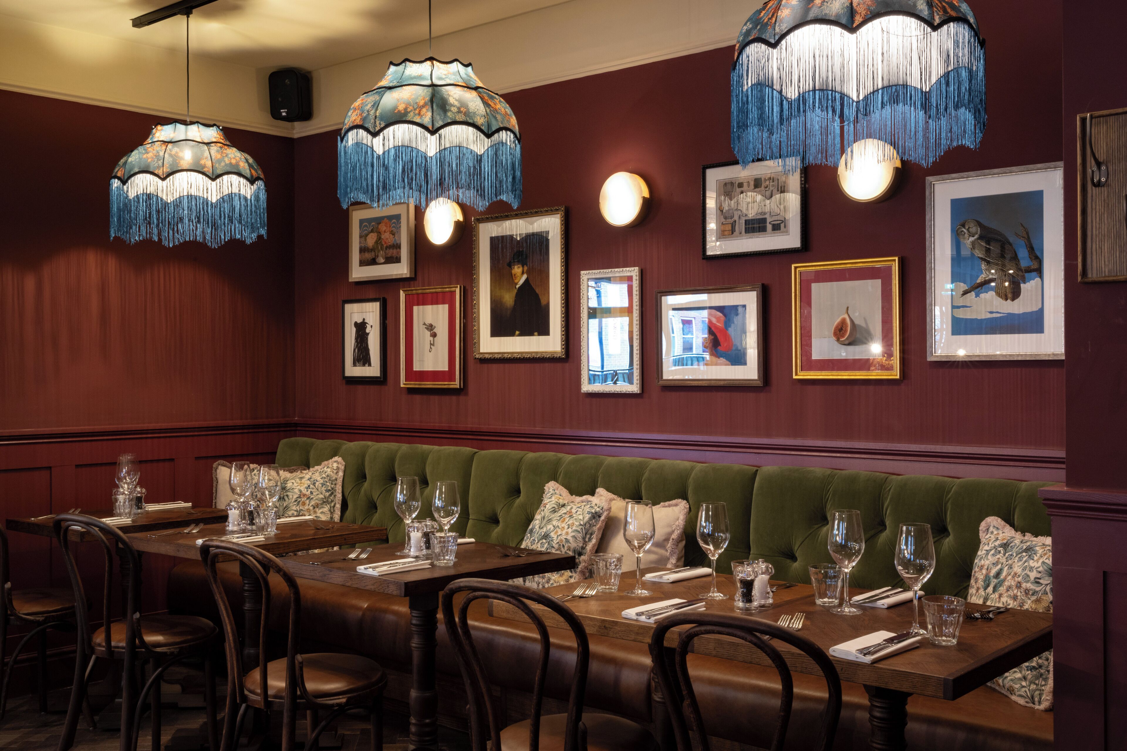 A restaurant with a long wooden table set for dining, a green upholstered bench, and framed artwork on the walls.
