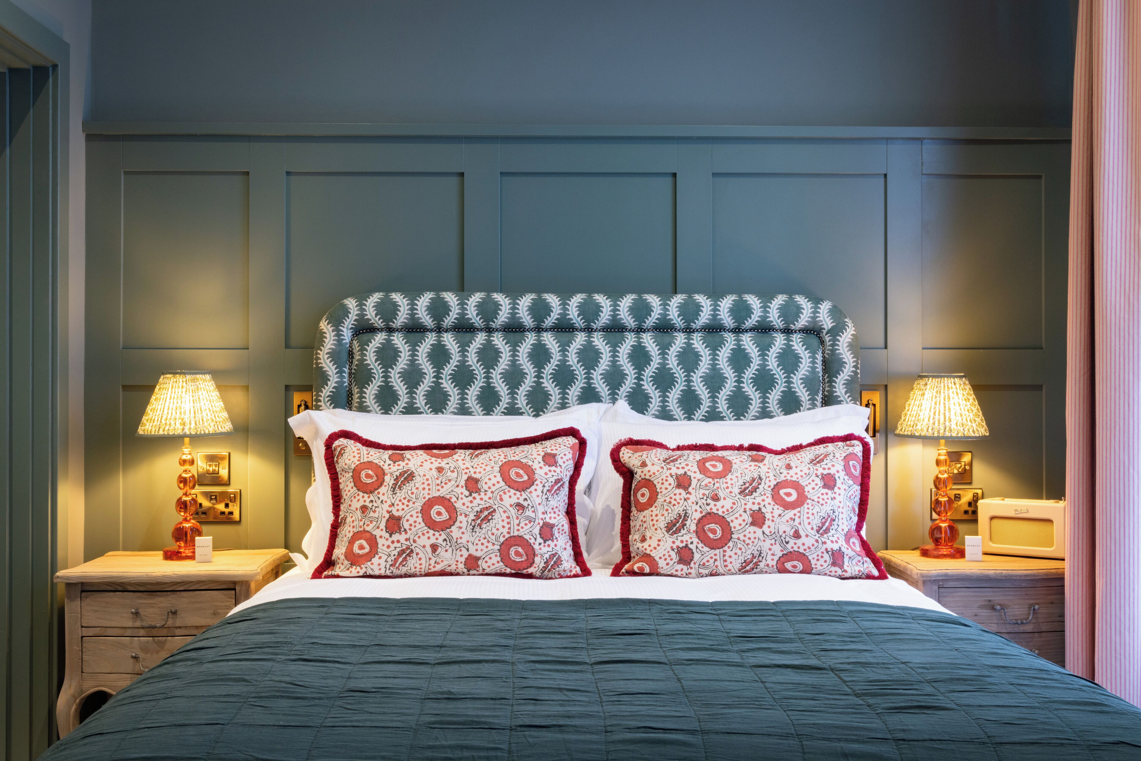 Una cama bien hecha con almohadones estampados, un cabecero con diseño geométrico y lámparas de noche sobre mesitas de madera.