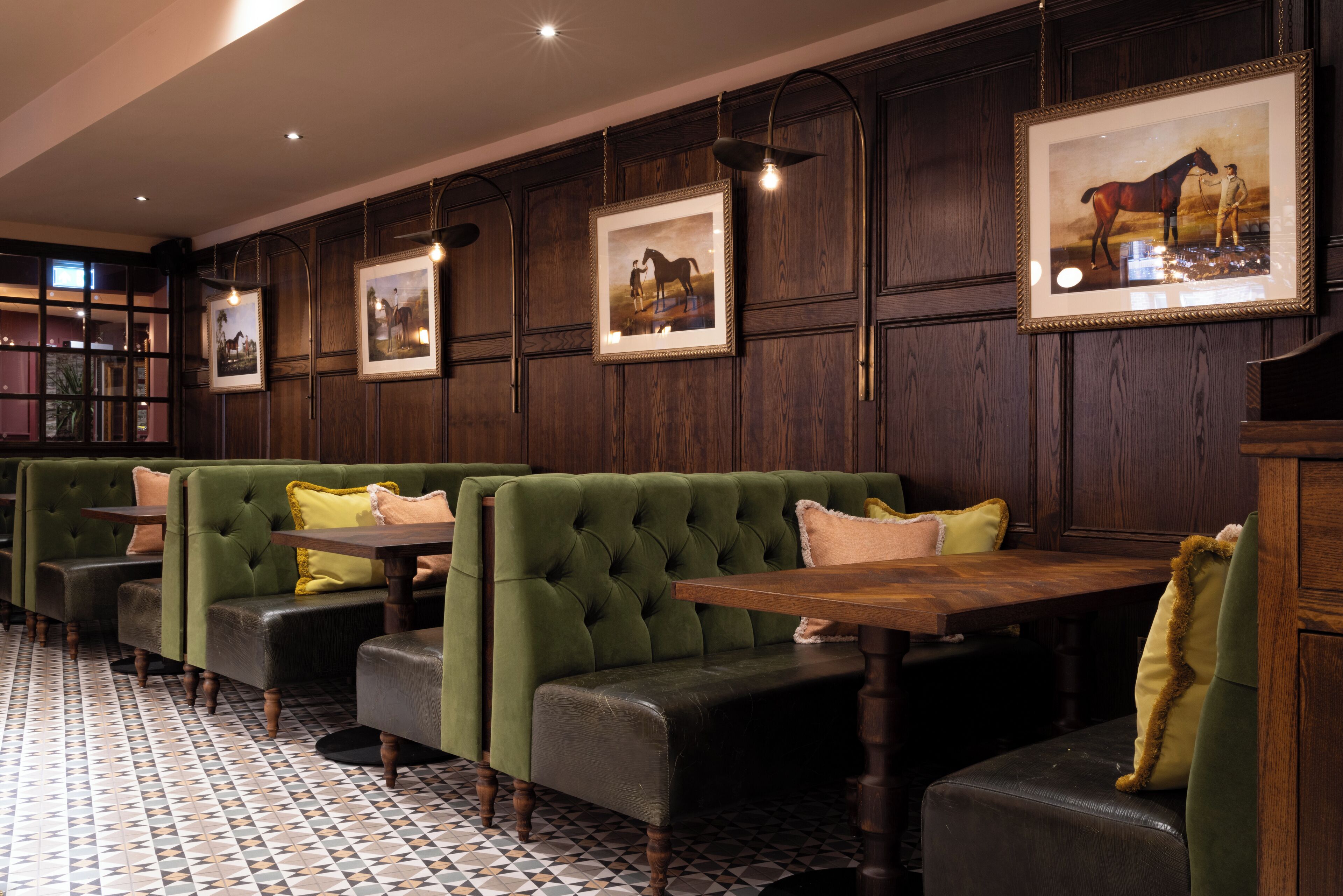 A restaurant with green upholstered booths, wooden tables, and framed pictures on the walls.
