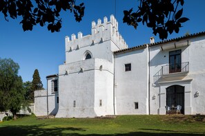 A white building with a tower, a balcony, and a small table with chairs. - Hospedium Hotel Cortijo Torre De La Reina (Guillena)
