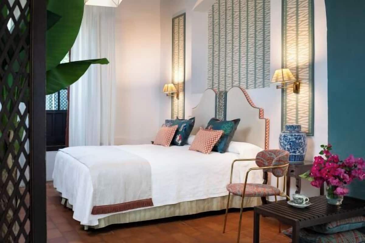 Une chambre à coucher bien rangée, avec un grand lit, deux lampes de chevet, un vase décoratif et une chaise.