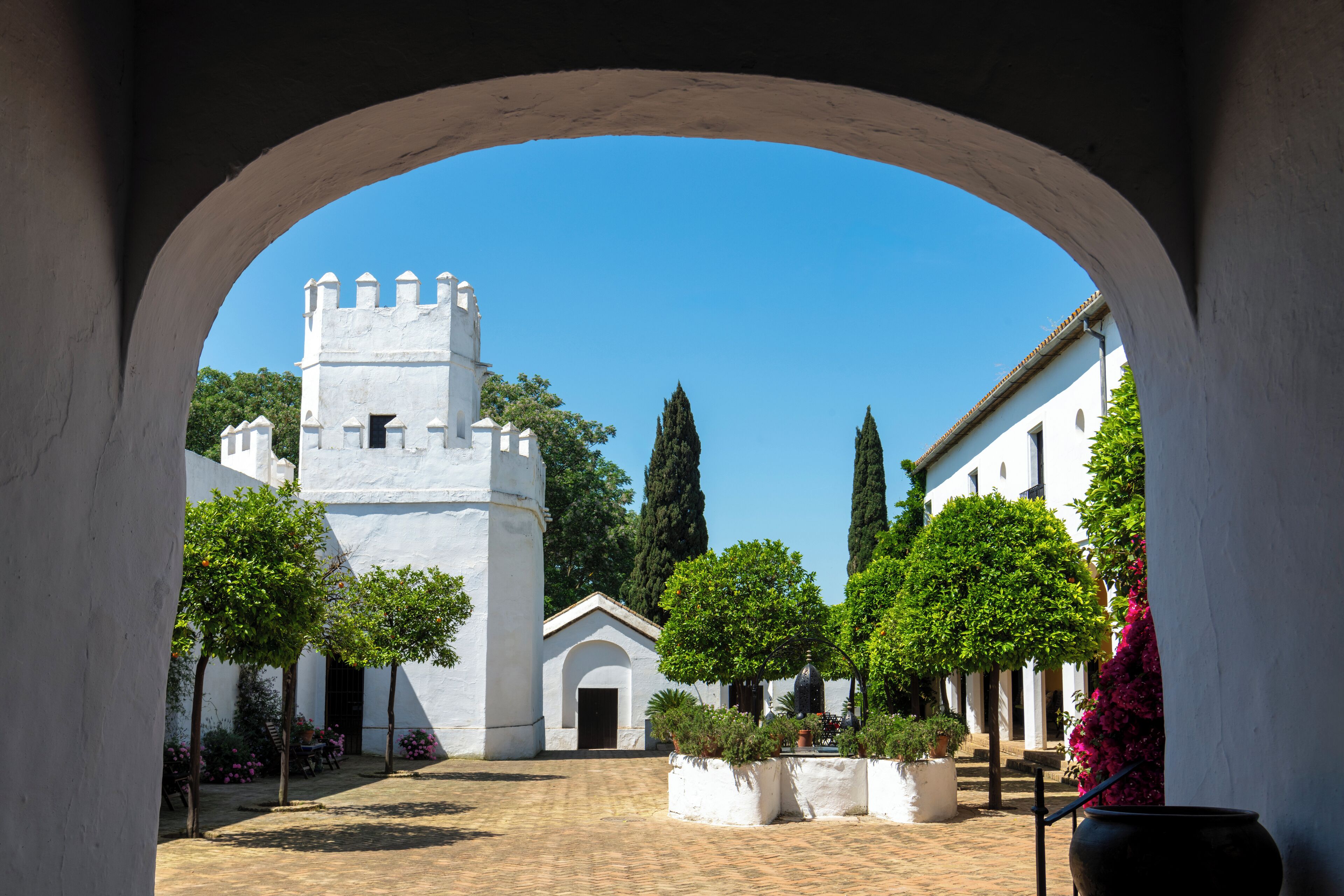 A courtyard with a white building, a tower, and a clear blue sky.