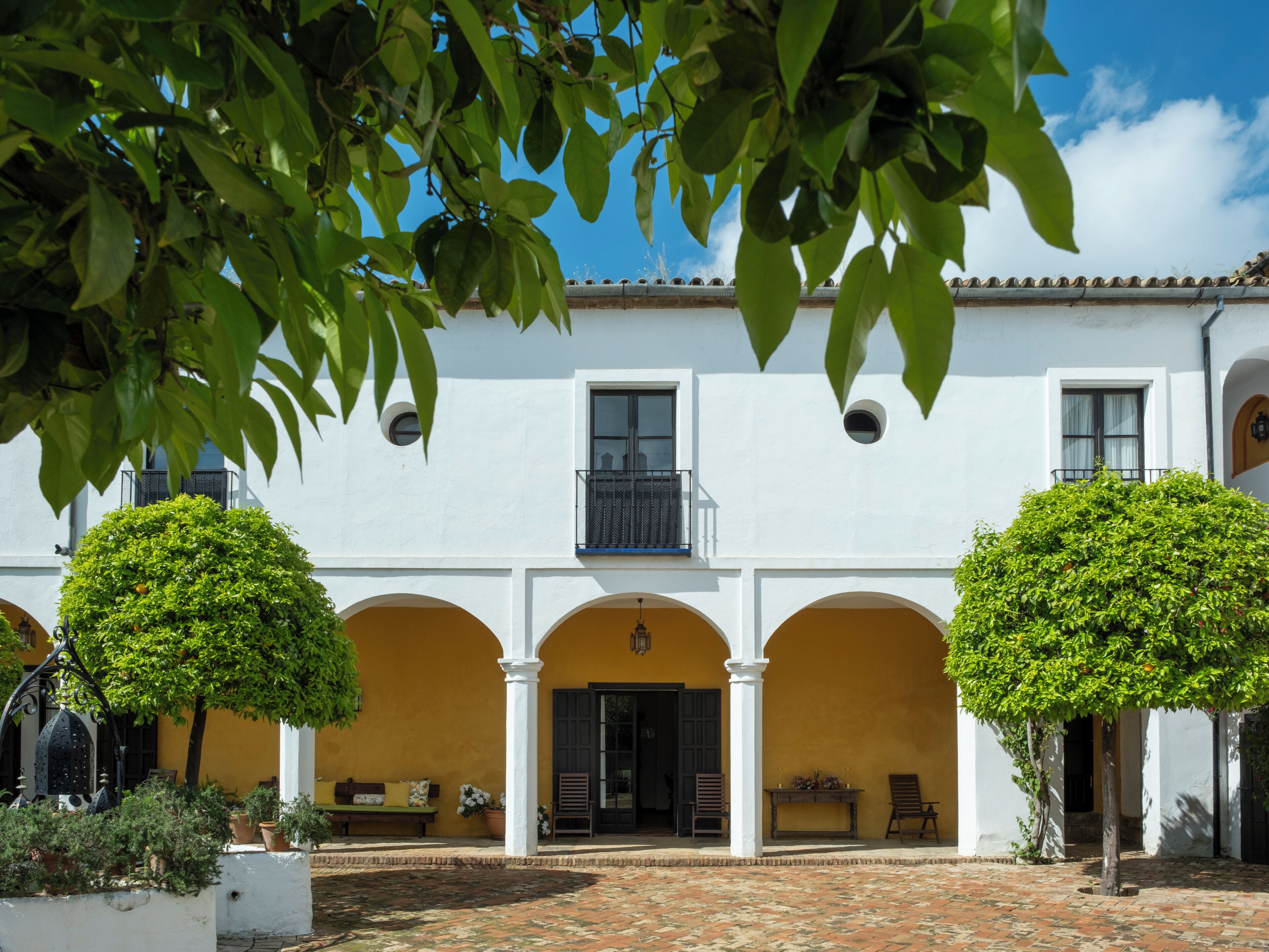 Un cortile con un edificio bianco caratterizzato da portali ad arco e un balcone.