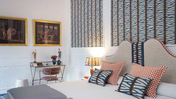 Un dormitorio ordenado con cama, almohadas, una mesita de noche, lámpara y dos cuadros enmarcados en la pared.