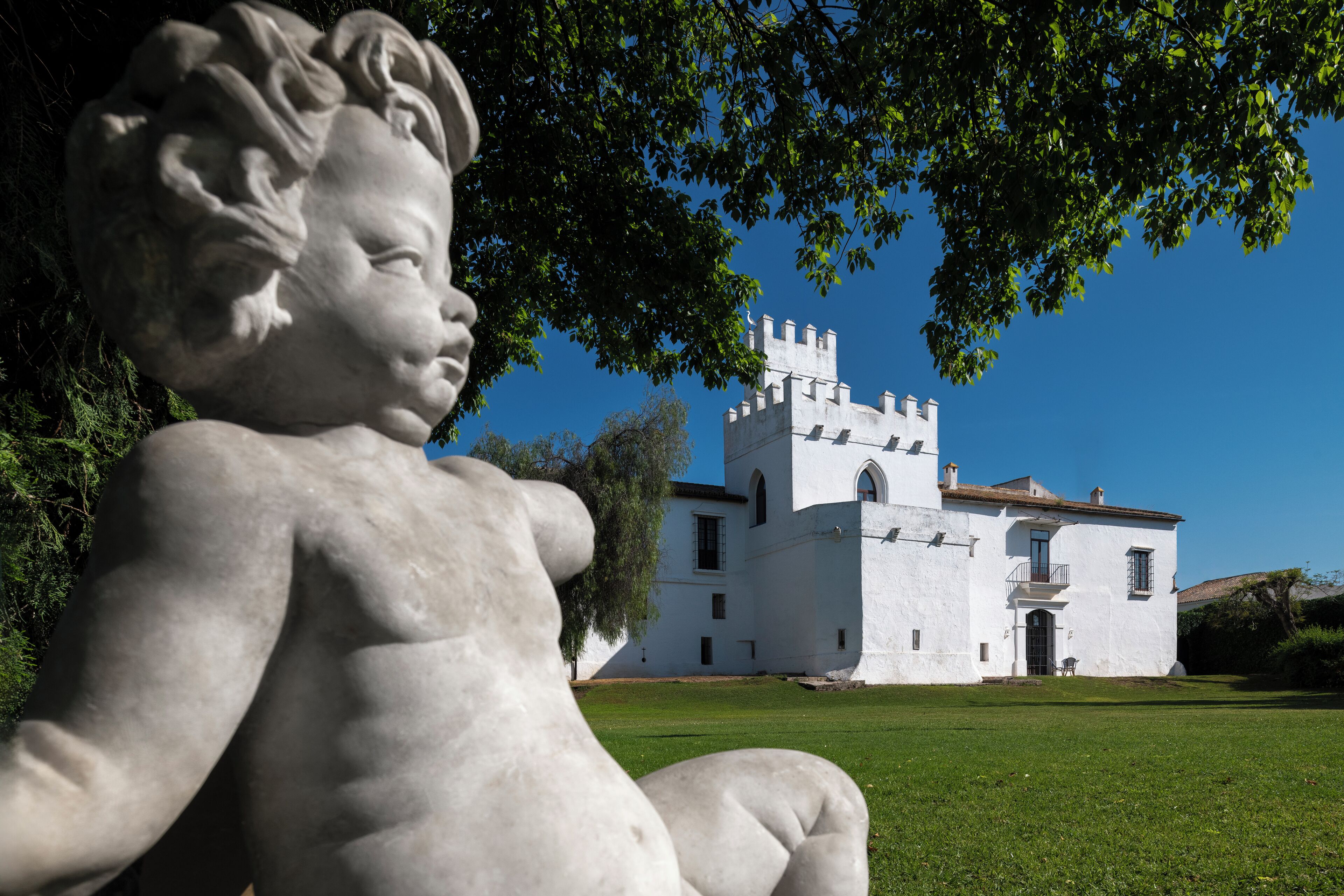 Una statua di un bambino in un parco, con un edificio bianco sullo sfondo.