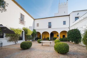 A courtyard with a central bench, surrounded by white buildings with yellow accents and a tiled roof. - Hospedium Hotel Cortijo Torre De La Reina (Guillena)
