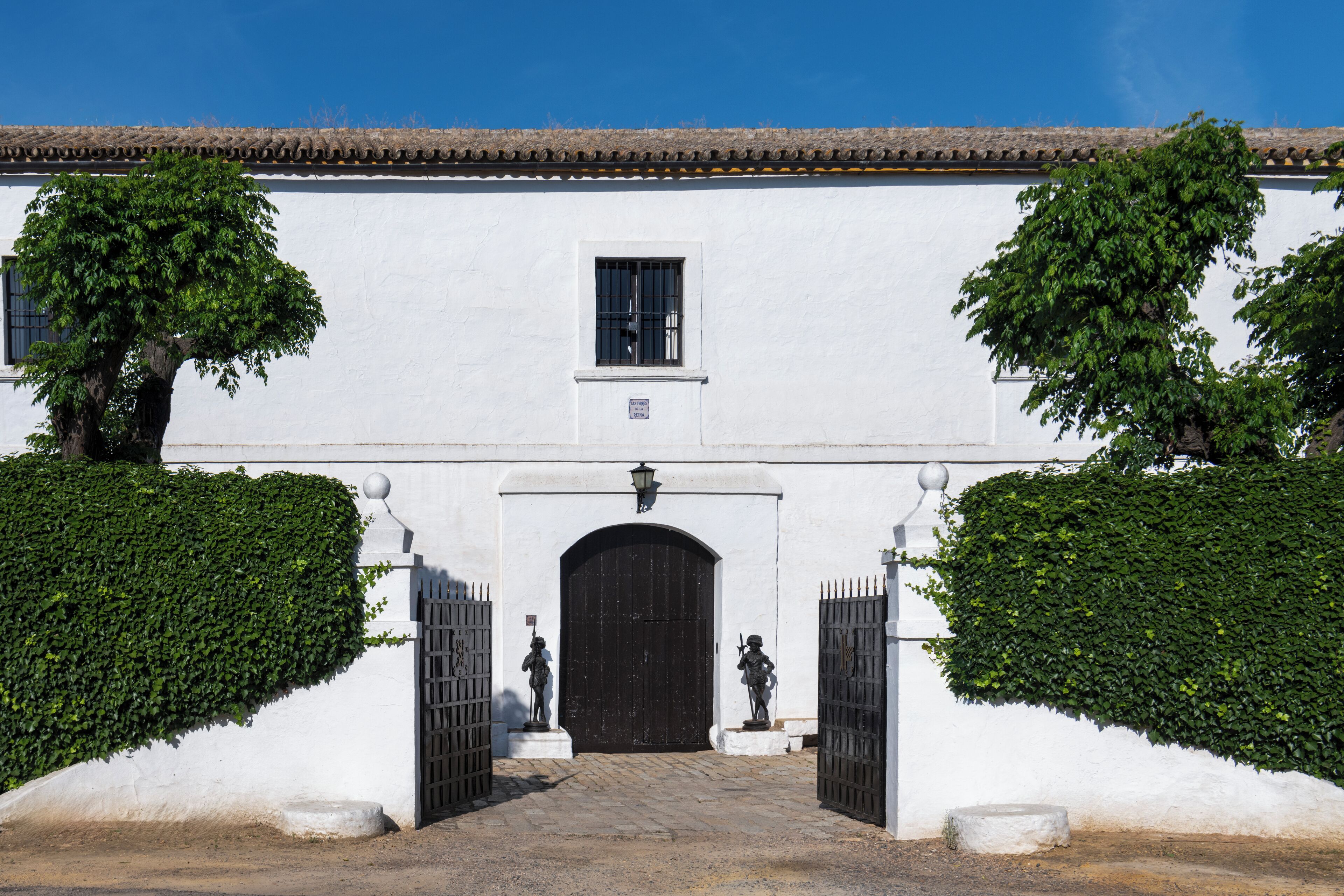 Un bâtiment blanc avec une porte noire, deux statues et un toit recouvert de tuiles.